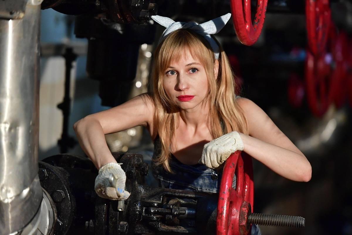 Femme en combinaison usagère manipulant une manivelle rouge dans un environnement industriel Femme en combinaison usagère manipulant une manivelle rouge dans un environnement industriel