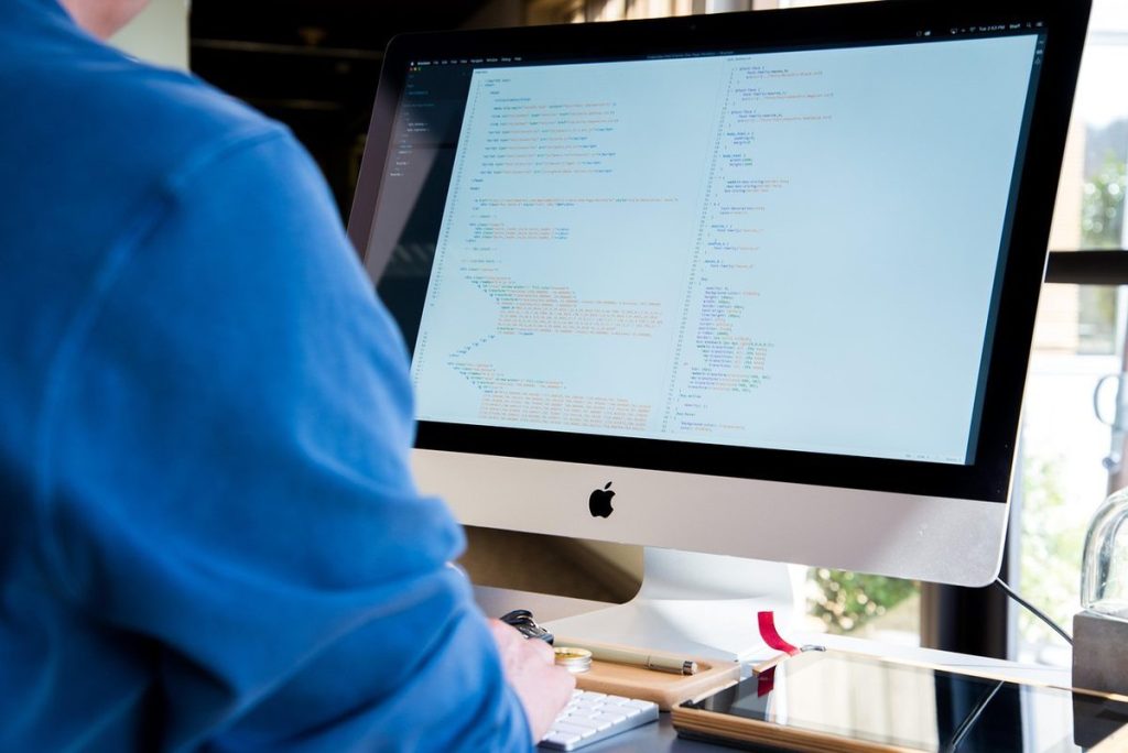 Individu en bleu devant un iMac affichant du texte, lumière ambiante