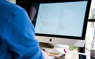 Individu en bleu devant un iMac affichant du texte, lumière ambiante