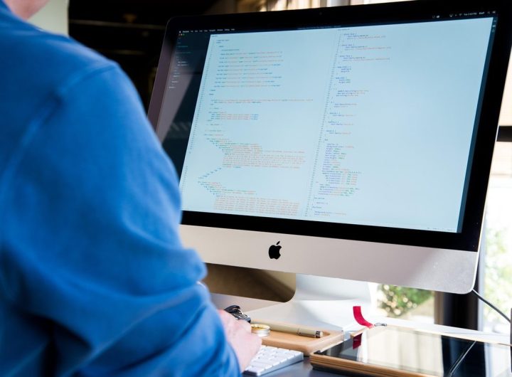 Individu en bleu devant un iMac affichant du texte, lumière ambiante