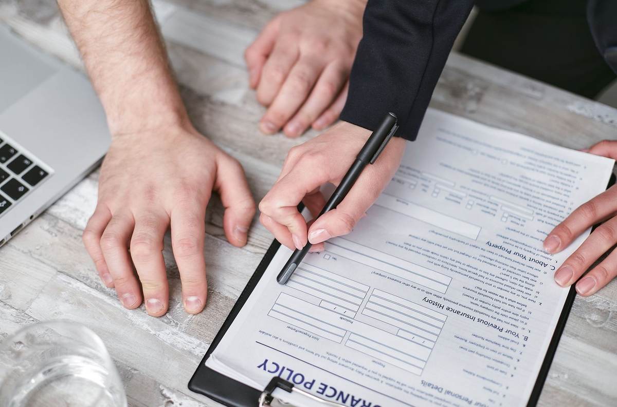Des mains signant un document sur une table avec un ordinateur et un verre d'eau