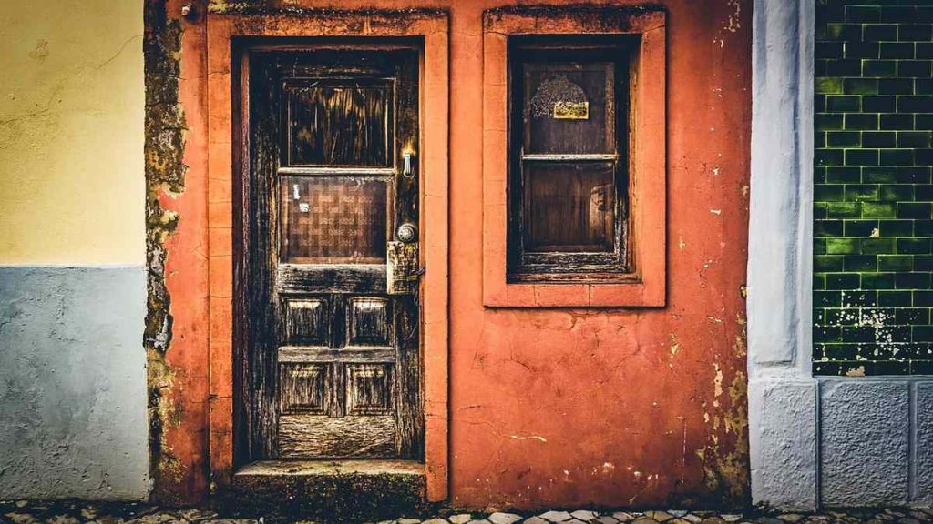 Une porte en bois usée à côté d'une fenêtre dans un mur orange