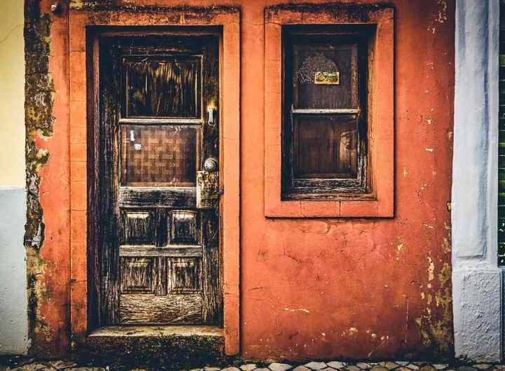 Une porte en bois usée à côté d'une fenêtre dans un mur orange