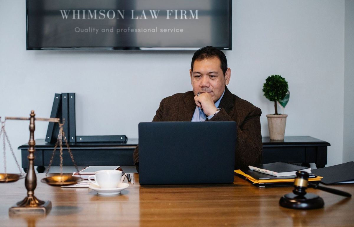 Homme assis devant un ordinateur dans un bureau avec des objets juridiques et un panneau de la firme