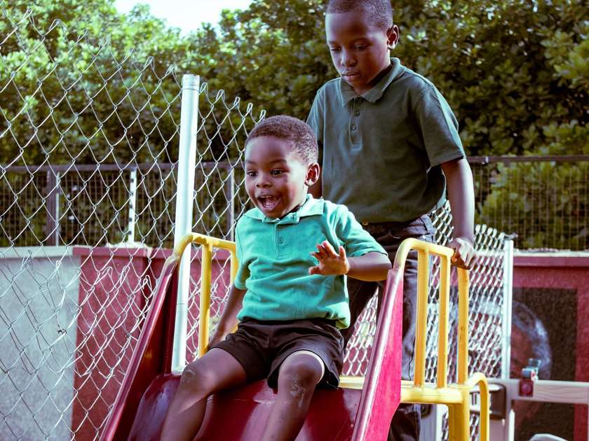 Enfants jouant sur une glissière rouge et jaune entourée d'un filet de sécurité, avec des arbres en arrière-plan