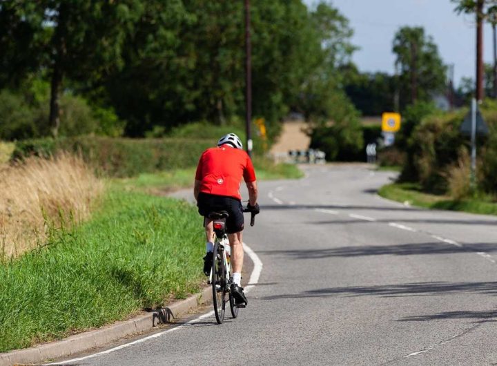 Cycliste sur route, casque, gants, arbres, buissons, panneau signalétique