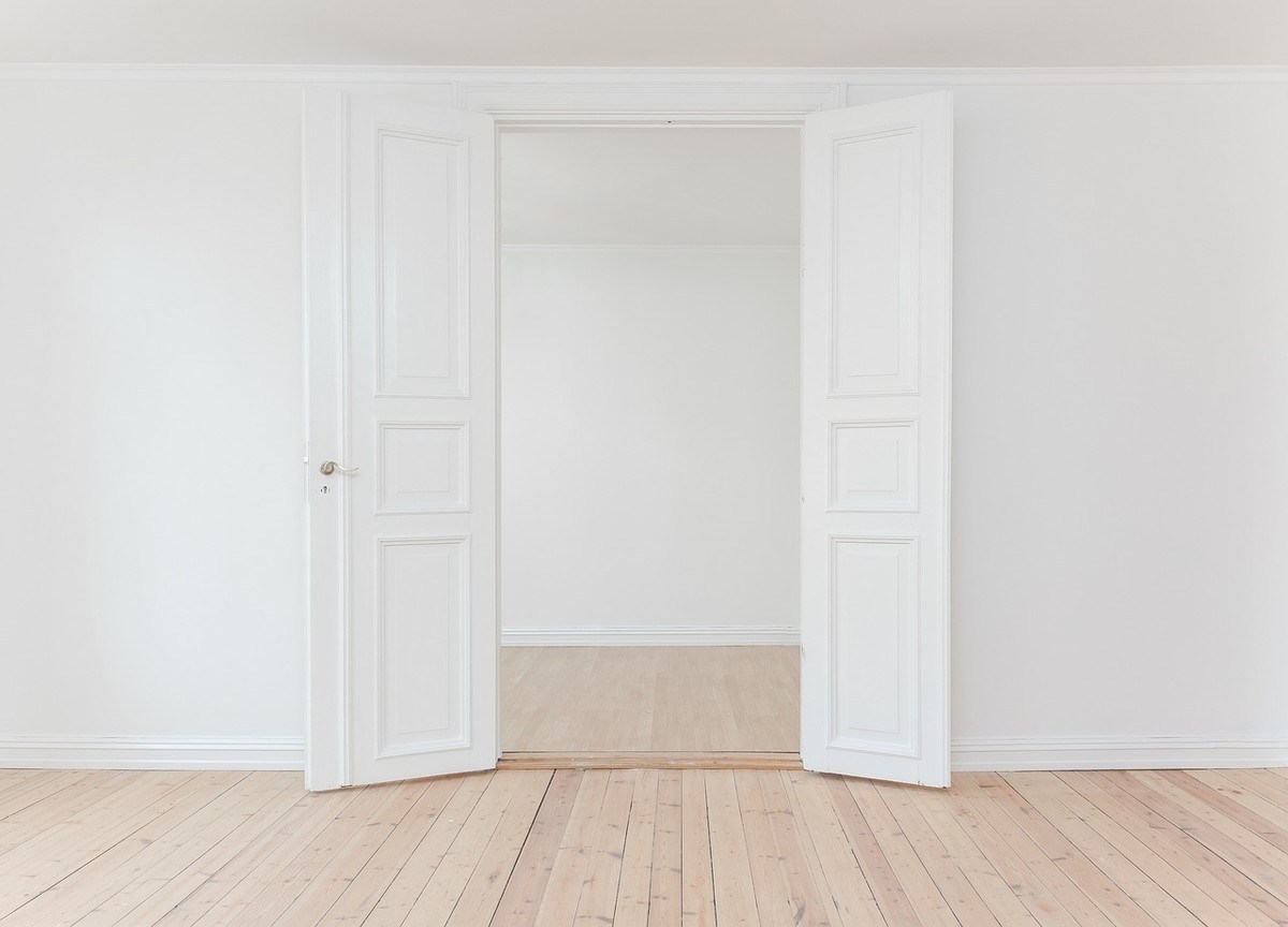 Deux portes blanches à panneaux ouvertes sur un espace vide aux murs blancs et sol en bois