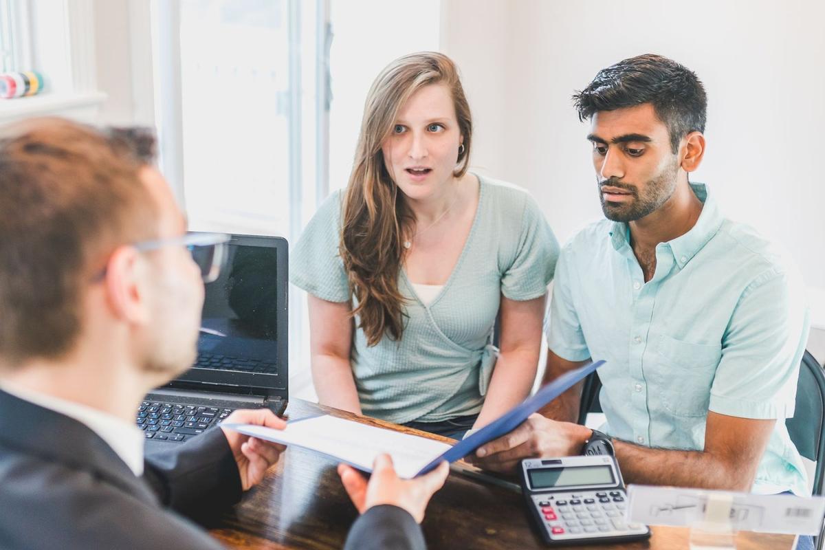 Trois personnes discutant de documents sur un bureau avec ordinateur et calculatrice