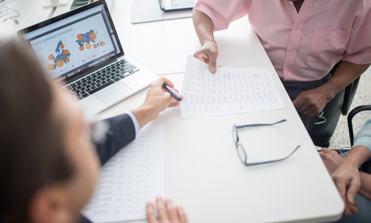 Trois personnes discutent autour d'un ordinateur portable et de documents sur une table