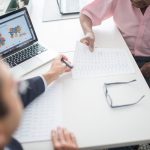 Trois personnes discutent autour d'un ordinateur portable et de documents sur une table