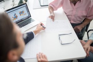 Trois personnes discutent autour d'un ordinateur portable et de documents sur une table