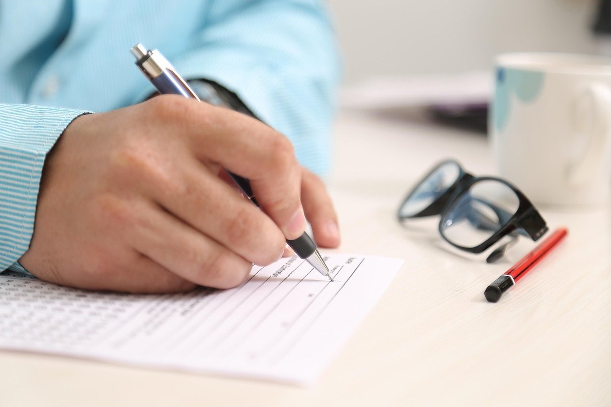 Mains écrivant sur feuille avec lunettes et stylo à côté Mains écrivant sur feuille avec lunettes et stylo à côté