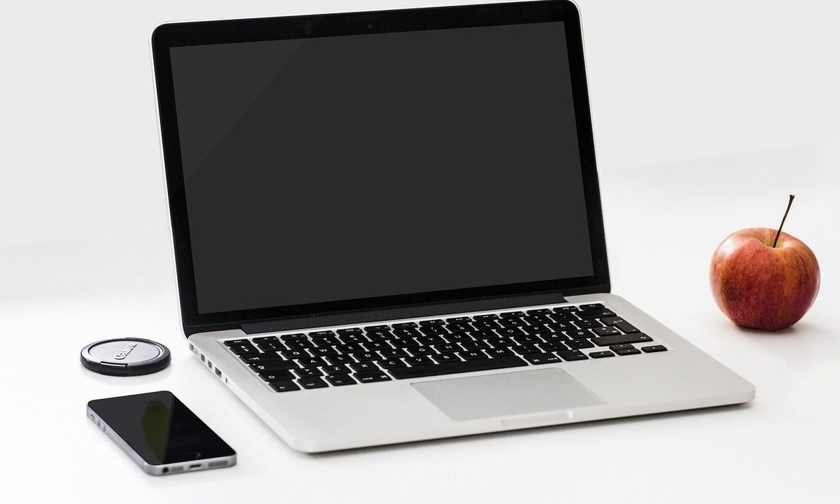 Laptop ouvert, smartphone, pomme et disque dur sur une table blanche