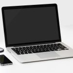 Laptop ouvert, smartphone, pomme et disque dur sur une table blanche