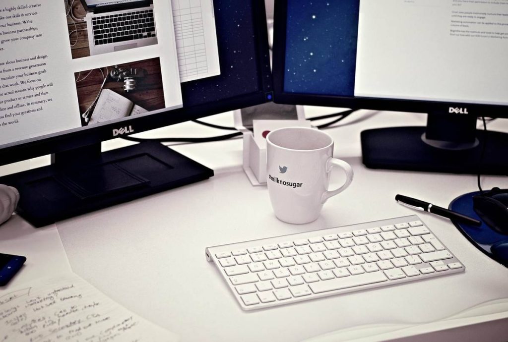 Bureau avec deux écrans Dell, clavier blanc, mug, stylo et documents épars