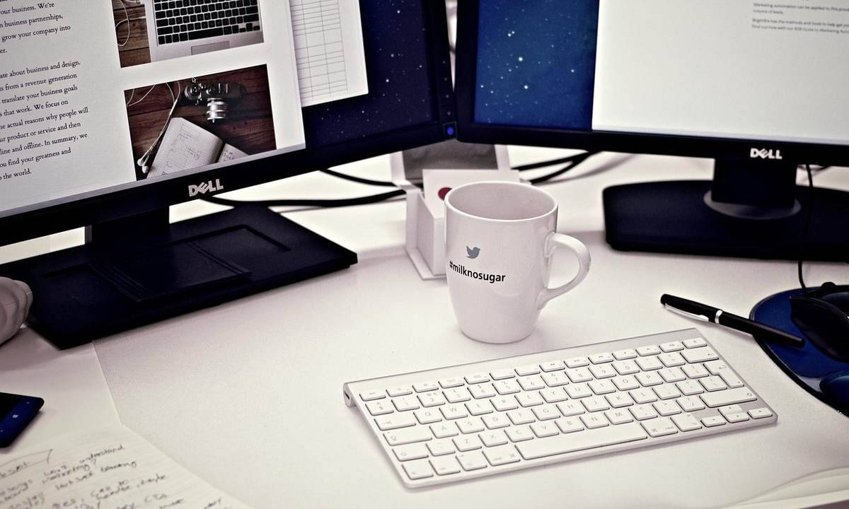 Bureau avec deux écrans Dell, clavier blanc, mug, stylo et documents épars