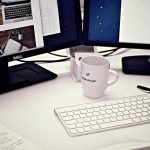 Bureau avec deux écrans Dell, clavier blanc, mug, stylo et documents épars