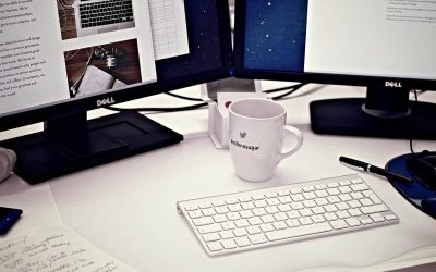Bureau avec deux écrans Dell, clavier blanc, mug, stylo et documents épars