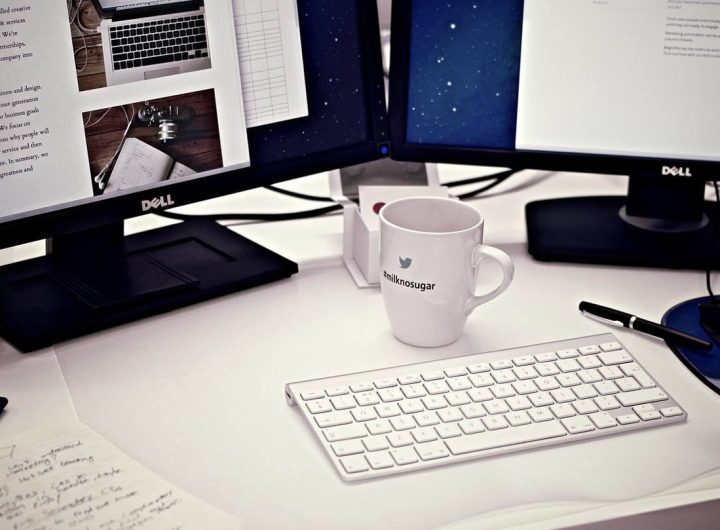 Bureau avec deux écrans Dell, clavier blanc, mug, stylo et documents épars