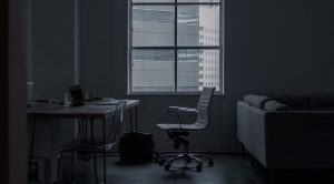 Salle sombre avec bureau, chaise, canapé, fenêtre et sac