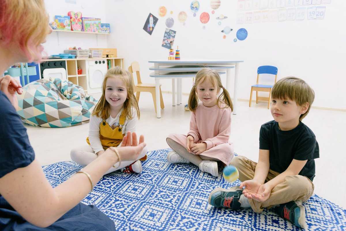 Enfants et adultes assis sur un tapis, jouant avec des objets dans une salle de classe Enfants et adultes assis sur un tapis, jouant avec des objets dans une salle de classe