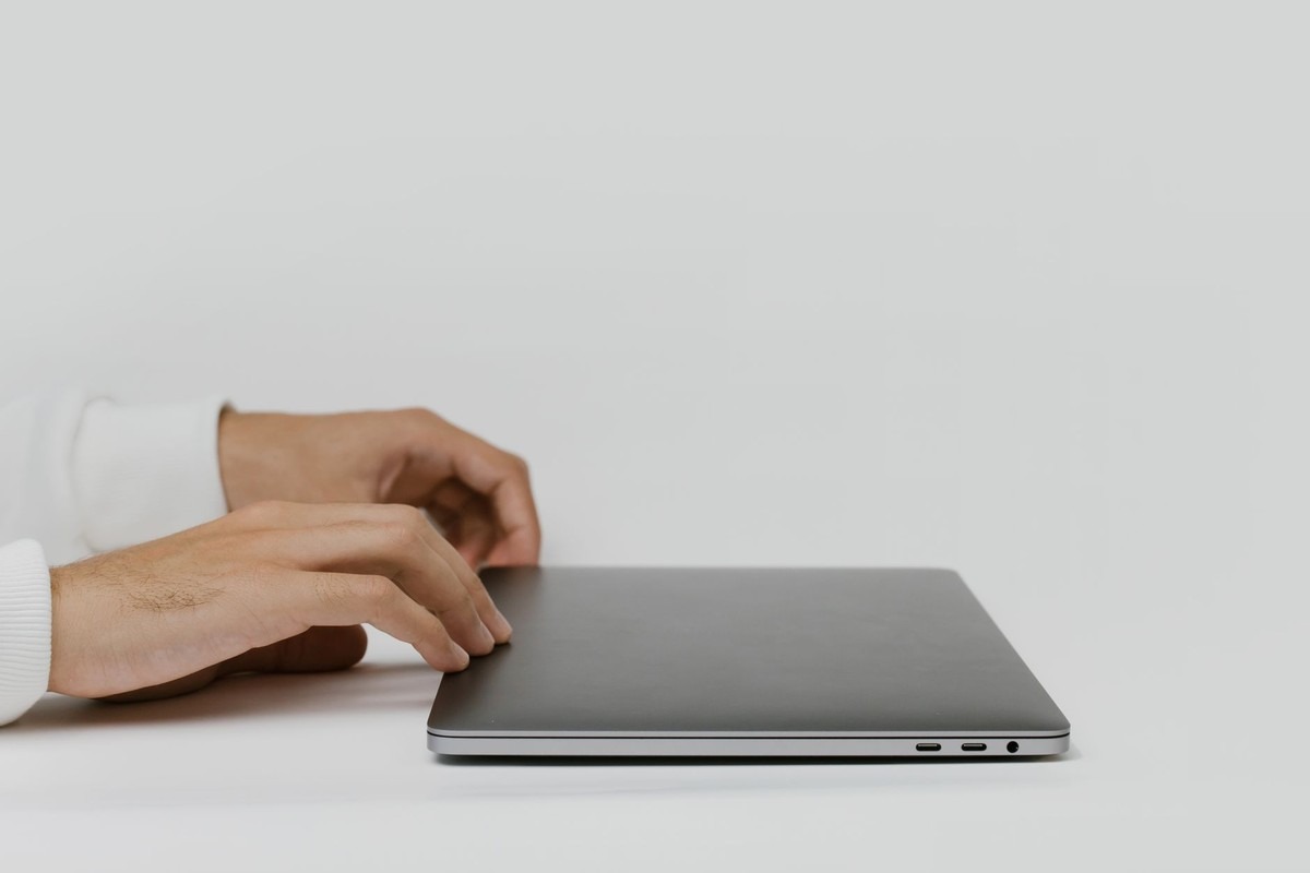 Mains d'un homme en chemise blanche utilisant un ordinateur portable gris sur un bureau blanc