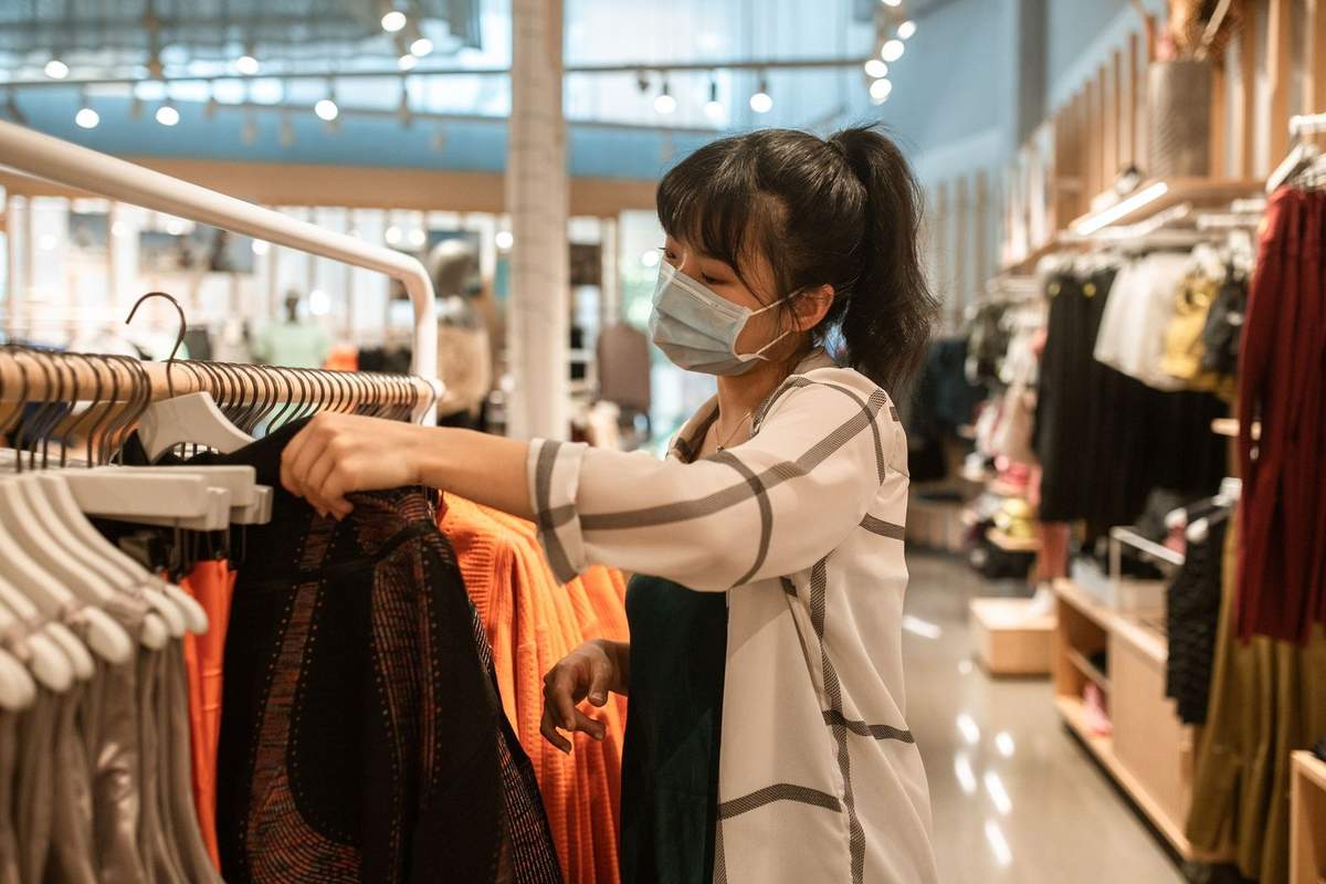 Femme masquée choisit des vêtements dans un magasin