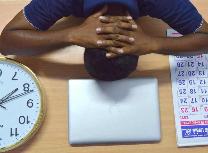 Homme endormi devant ordinateur, montre d'horloge, agenda sur bureau en bois
