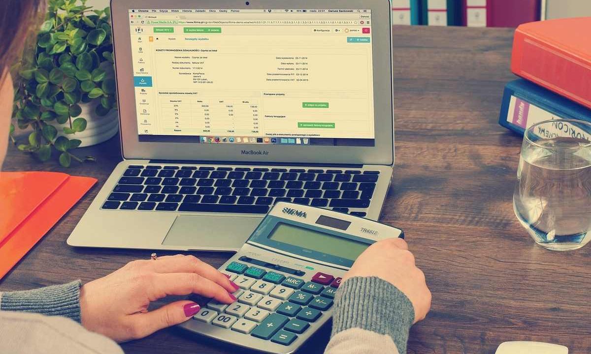 Person utilisant un ordinateur portable et une calculatrice sur une table en bois