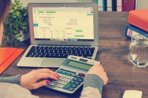 Person utilisant un ordinateur portable et une calculatrice sur une table en bois