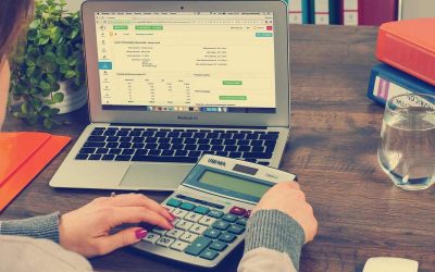 Person utilisant un ordinateur portable et une calculatrice sur une table en bois