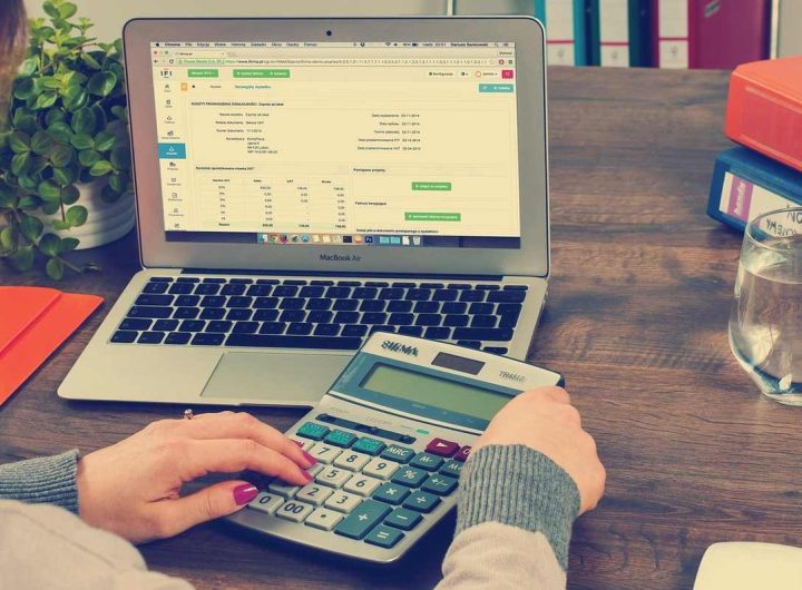 Person utilisant un ordinateur portable et une calculatrice sur une table en bois