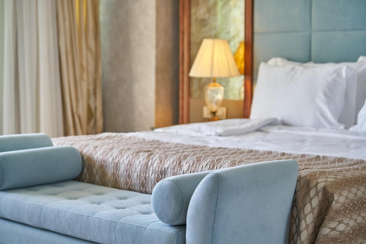 Un lit avec oreillers, coussin, lampe et banc dans une chambre Un lit avec oreillers, coussin, lampe et banc dans une chambre